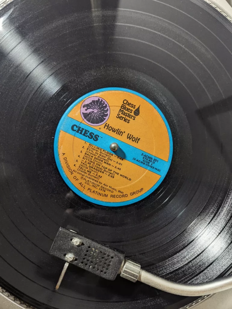 A black Howlin' Wolf vinyl record with an orange and blue Chess label spinning on a turntable under a tonearm.