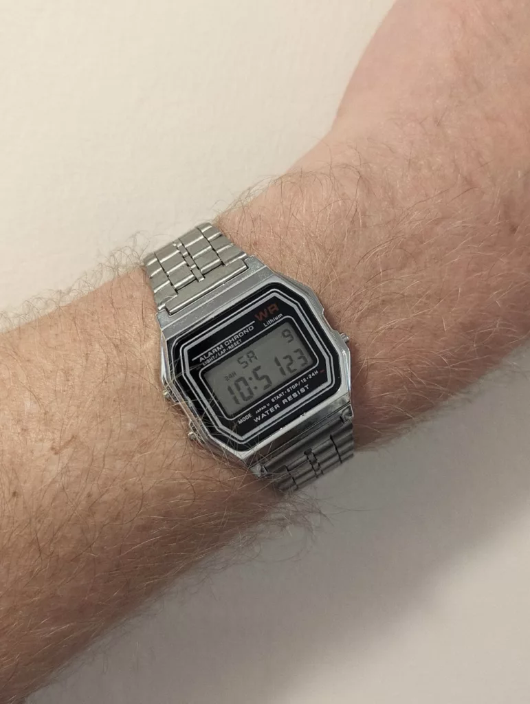 A silver digital alarm chronograph watch with a metal link strap on a wrist, displaying the time 10:51:23.