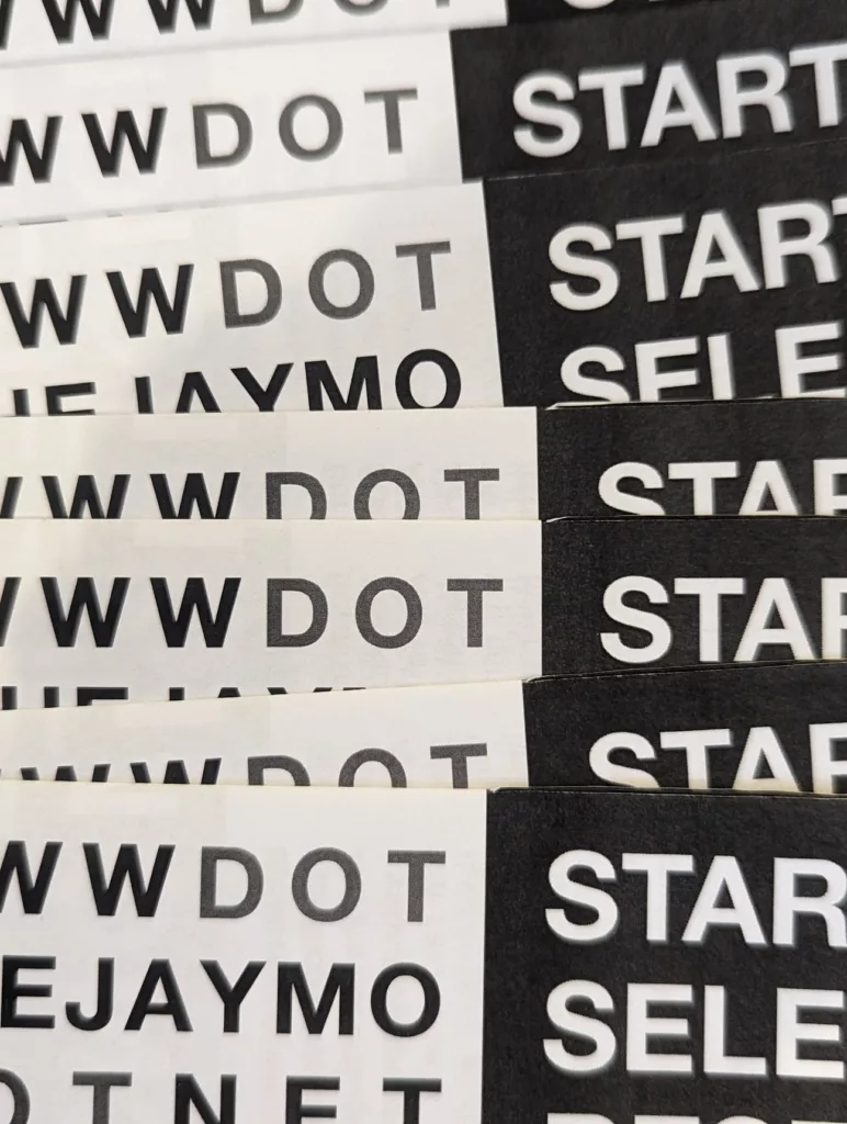 Close-up of stacked black and white stickers with bold sans-serif text reading WW DOT, EJAYMO, and START.