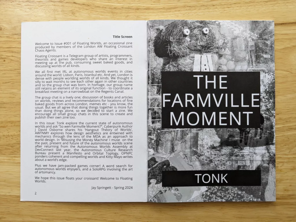 Open zine on a wooden table. Left page: intro for Floating Worlds #001. Right page: 'THE FARMVILLE MOMENT' by 'TONK' over a grainy straw figure.