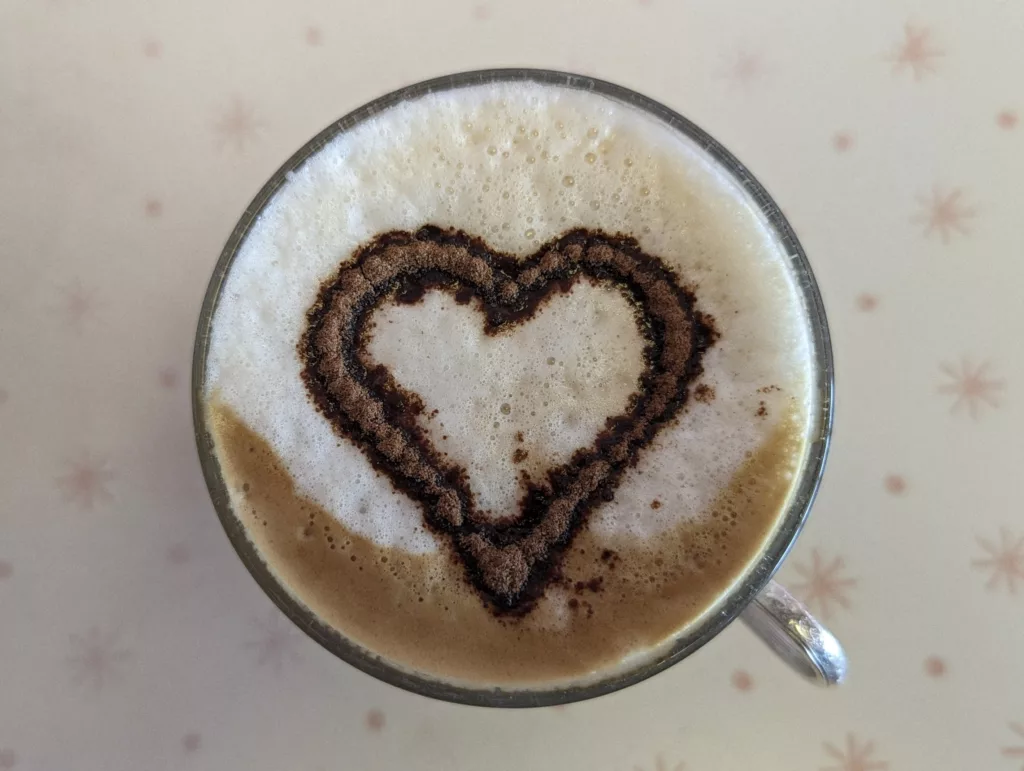 Cocoa powder heart dusted on the thick foam of a coffee in a clear glass mug, viewed from above on a star-patterned surface.