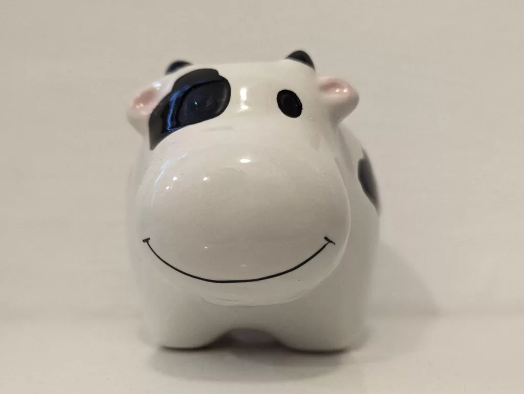 Close-up of a white ceramic cow figurine with black spots and a simple black line smile on its large, rounded snout.
