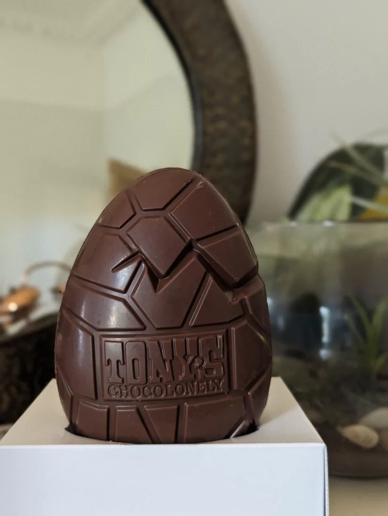 A Tony’s Chocolonely milk chocolate Easter egg with deep geometric ridges, embossed with the brand logo and resting in a white box.