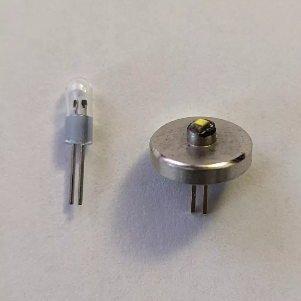 A clear miniature bulb and a circular metal component with a tiny yellow center, both with two metal pins, against a white background.