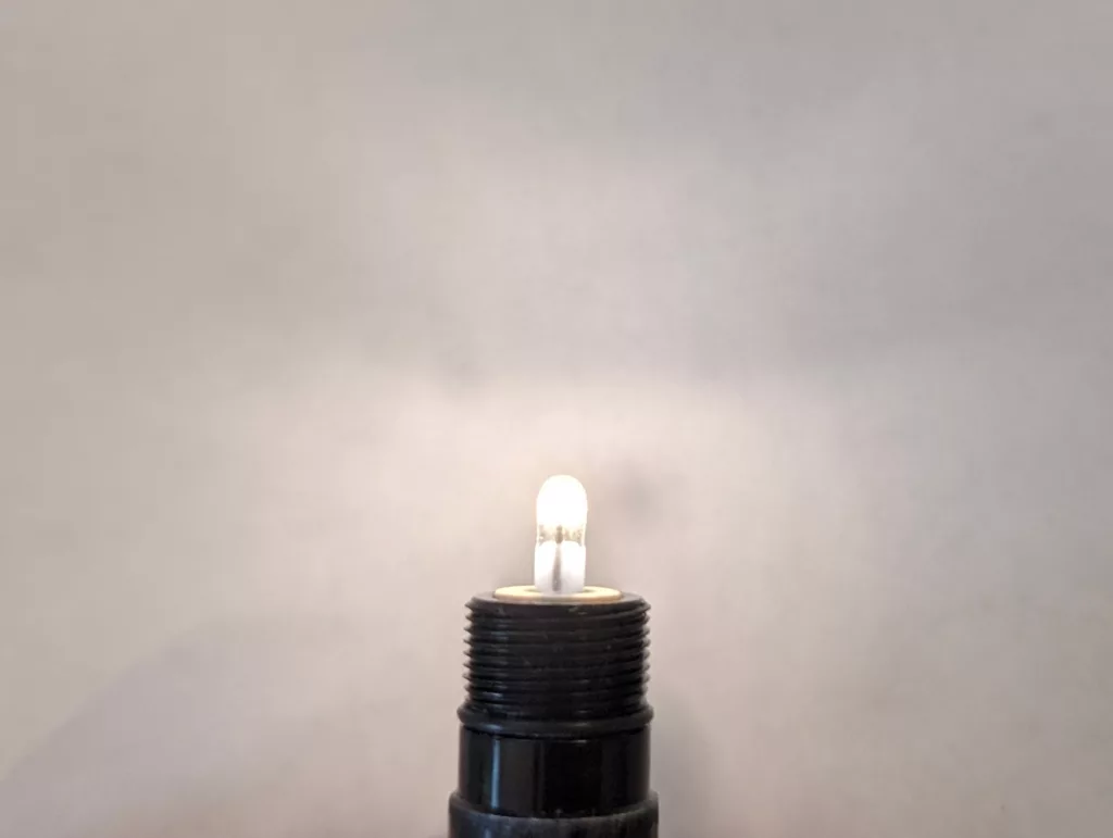 A small glowing light bulb atop a black threaded base against a plain grey background.