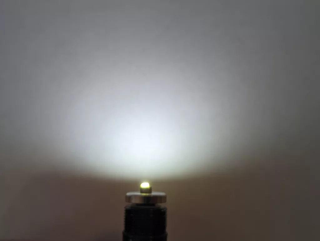 A small yellow LED on a threaded metal base casting a bright, diffuse white beam upwards against a plain background.