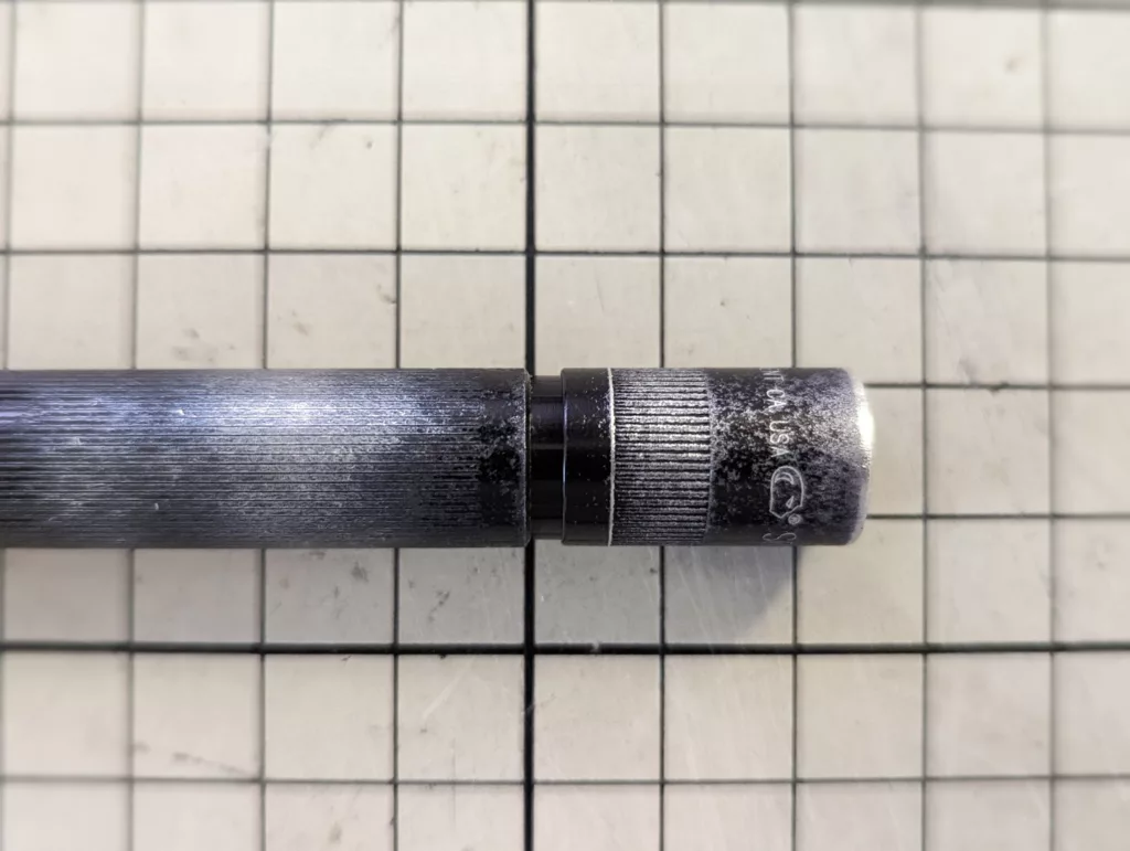Close-up of a weathered black metal handle with a knurled section resting horizontally on a cream-colored grid cutting mat.