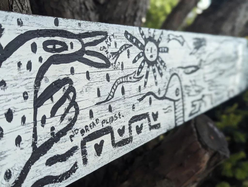 Black ink folk art on a white wood plank featuring a bird, a sun, and hand-written text: HEY, CAN I EAT YOU? and NO BREAD PLEASE.