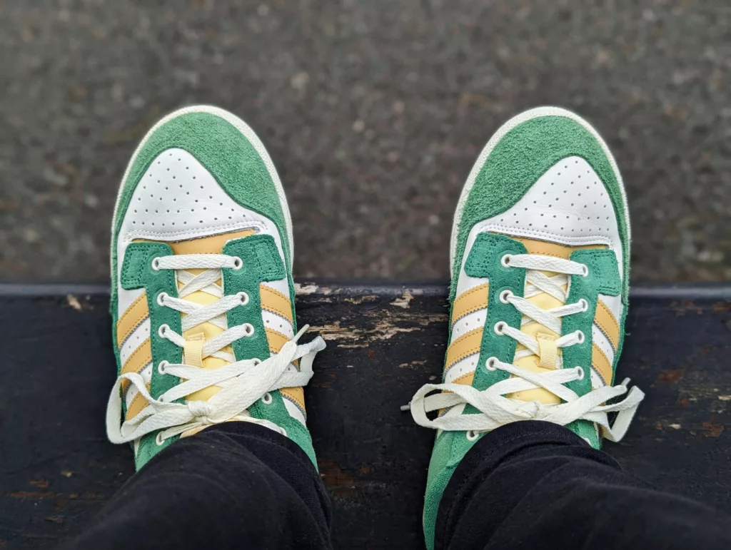 Green, yellow, and white suede sneakers with cream laces, viewed from above while resting on a weathered dark ledge.