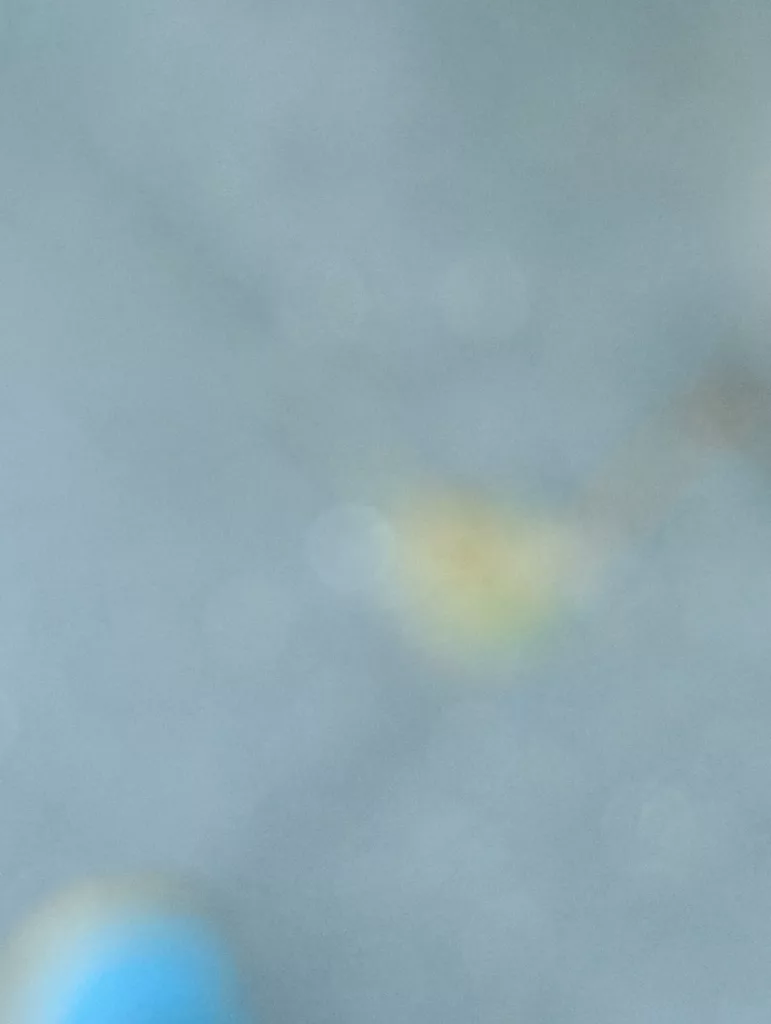 Abstract out-of-focus bokeh with a soft yellow glow on a pale blue background and a bright blue spot in the bottom left corner.