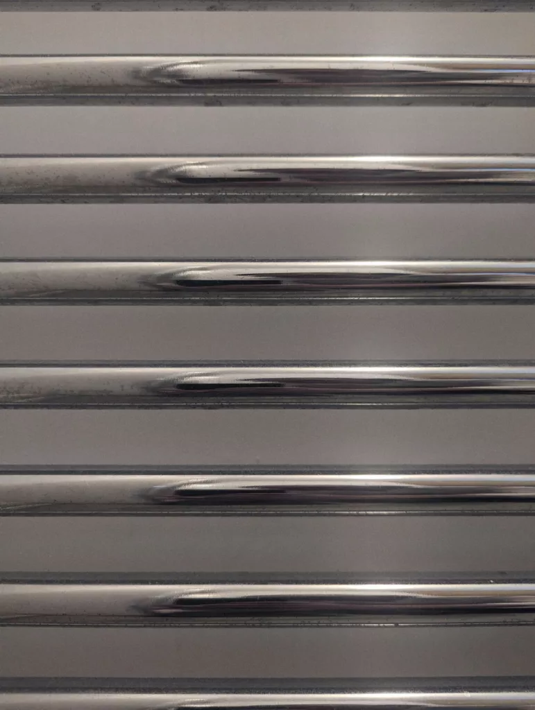 Horizontal polished chrome rails of a towel radiator against a light grey background.