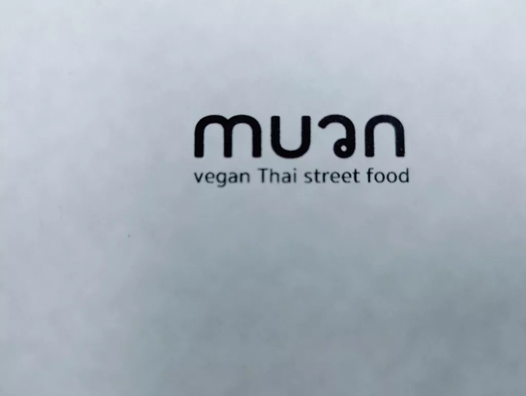 Black rounded typography for muan with the tagline vegan Thai street food underneath on a white surface.