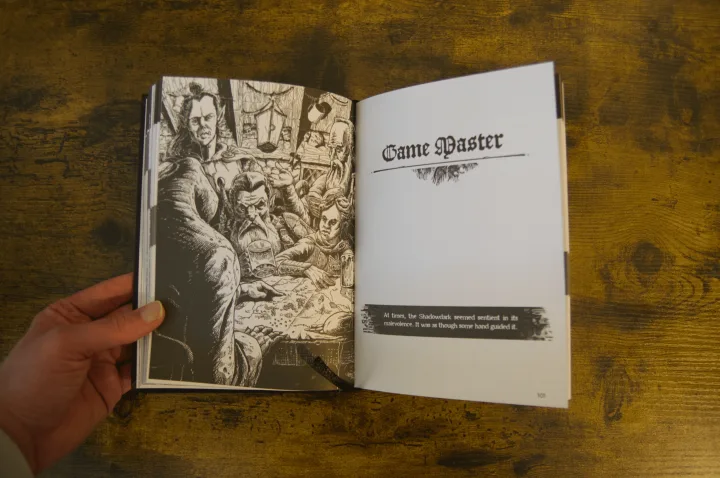 An open book on a wooden table showing a detailed fantasy illustration and a page titled Game Master in a black gothic typeface.