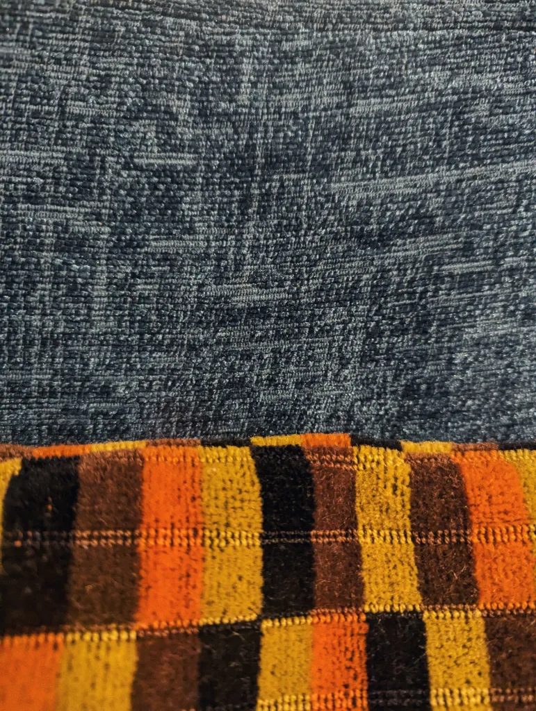 A dark blue woven fabric sits above a patterned textile featuring bold vertical stripes of orange, yellow, black, and brown.