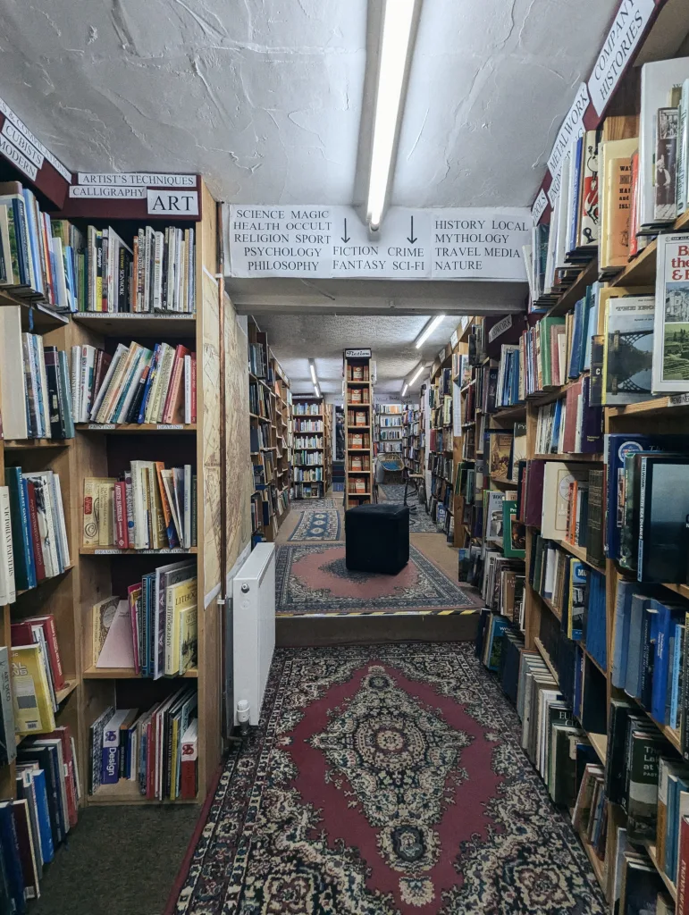 Narrow bookstore aisles of Michael's Bookshop in Ramsgate with floor-to-ceiling shelves, patterned rugs on the floor, and paper signs for categories like Art, Science, and Fiction.