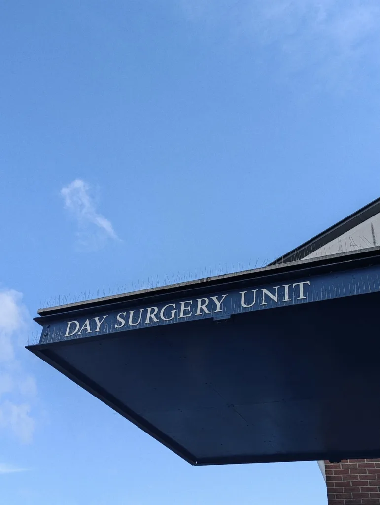 A dark blue Day Surgery Unit entrance awning with bird spikes on top, set against a bright blue sky.