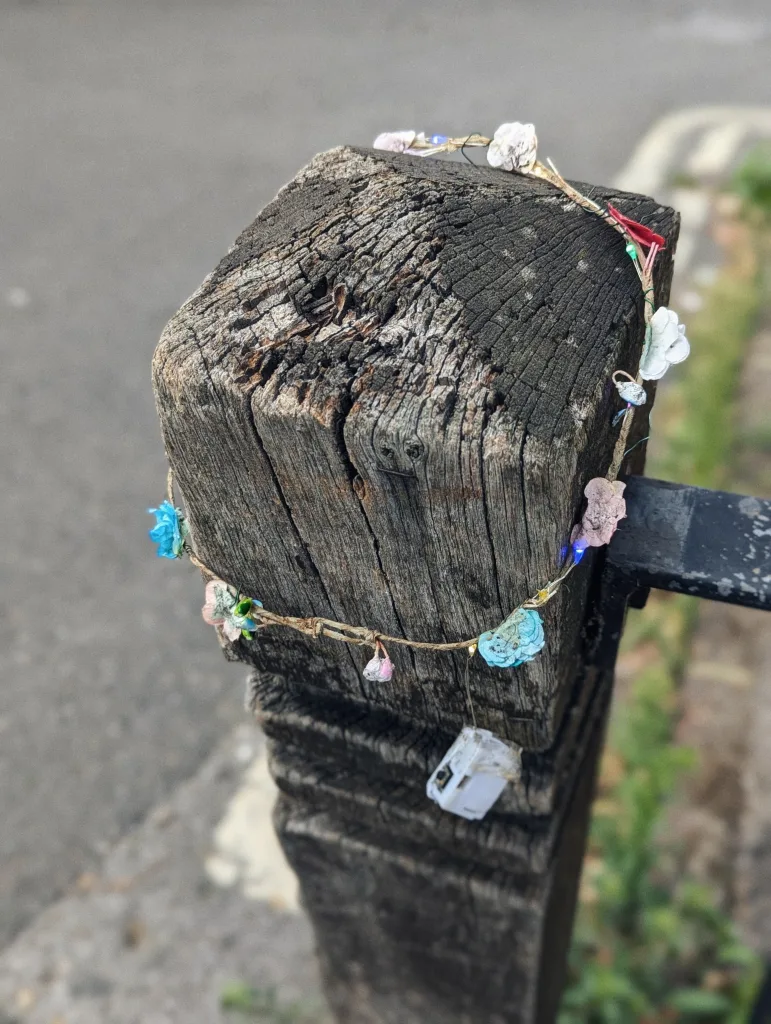 A floral light-up headband with pink and blue blossoms wrapped around a weathered wooden post.