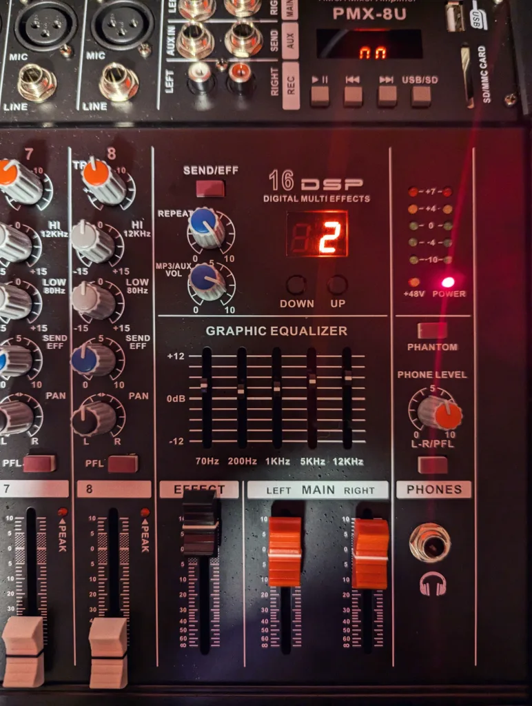 A PMX-8U audio mixing console with grey and orange knobs, a five-band graphic equalizer, and a red digital display showing the number two.