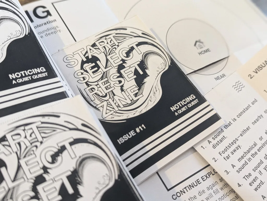 Copies of Start Select Reset Zine Issue #11 titled Noticing A Quiet Quest, with abstract black and white artwork and sensory exploration prompts.