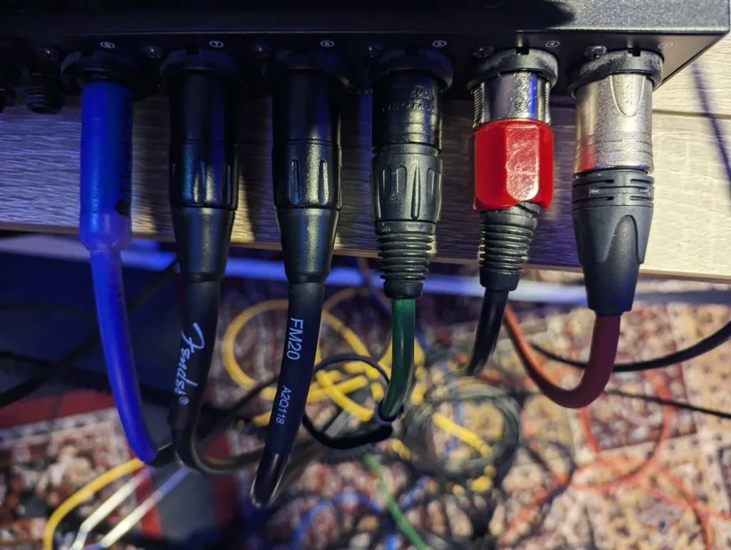 A row of six diverse XLR and audio cables in blue, black, and red, plugged into the rear ports of a black audio interface.