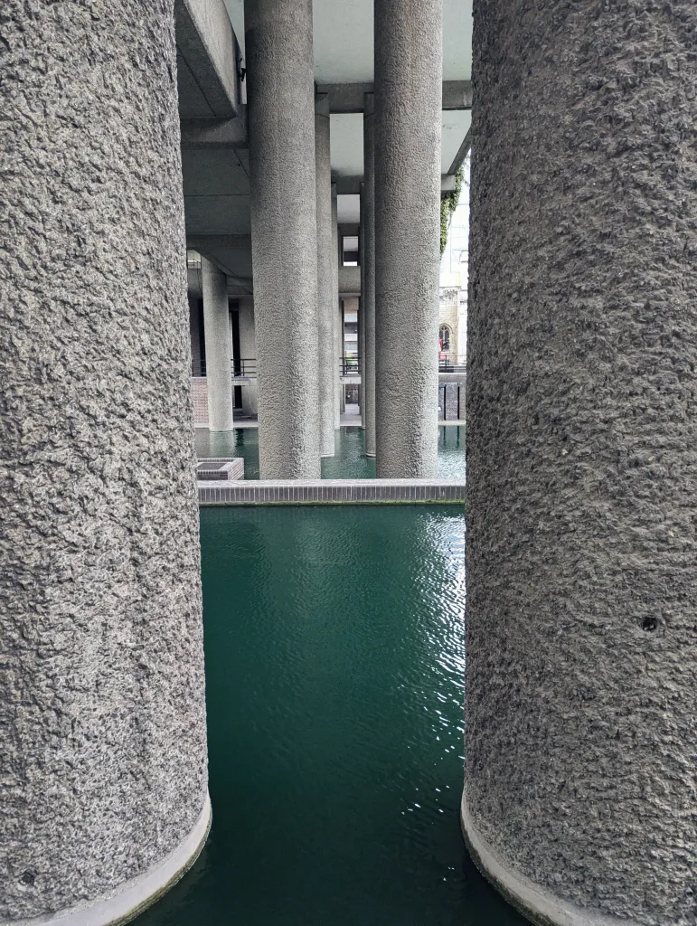 Massive textured concrete pillars rising from a turquoise pool at the Barbican Estate.