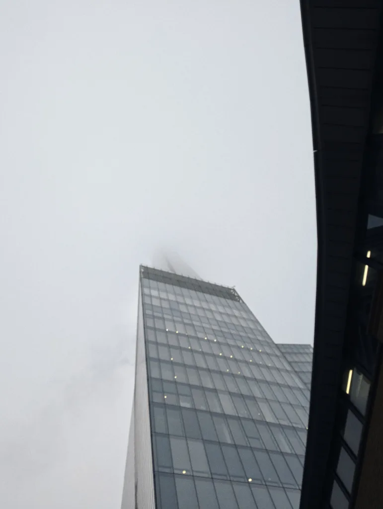 The glass spire of The Shard skyscraper in London disappearing into thick grey fog on an overcast day.