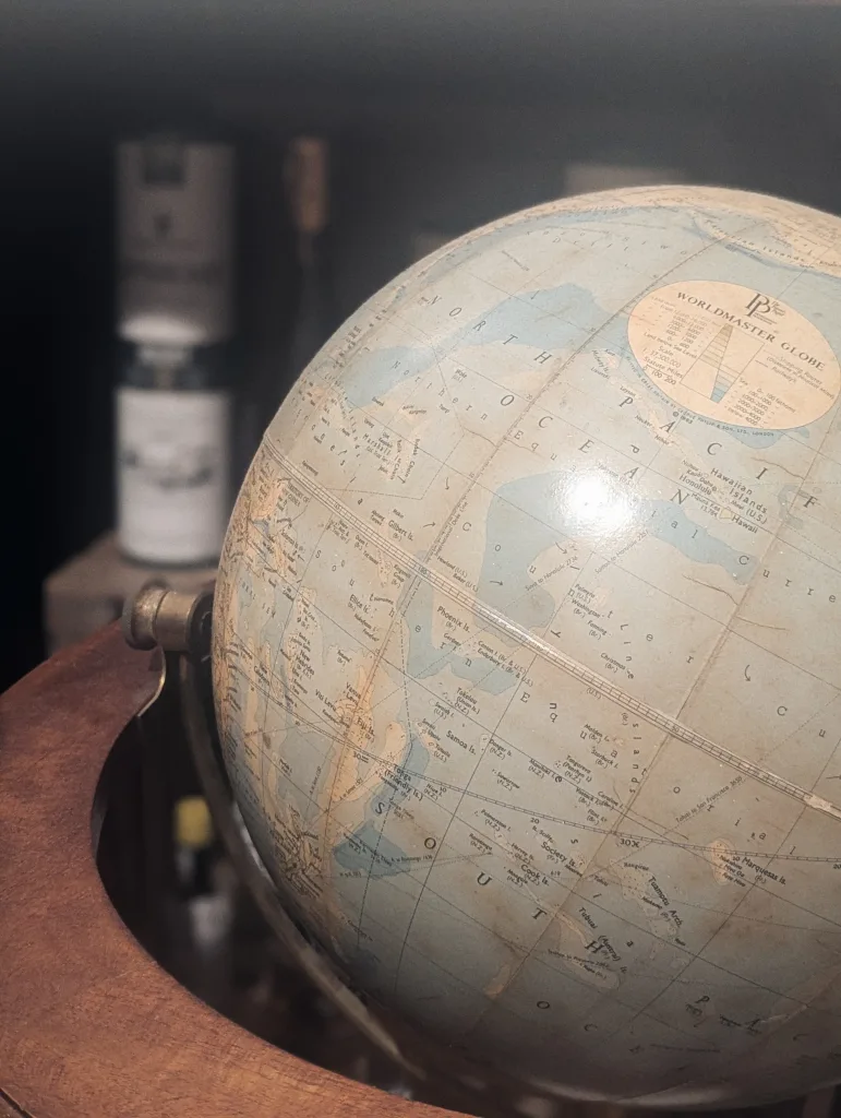 A close-up of a vintage Worldmaster Globe focused on the Pacific Ocean, resting in a wooden cradle with a blurred background.