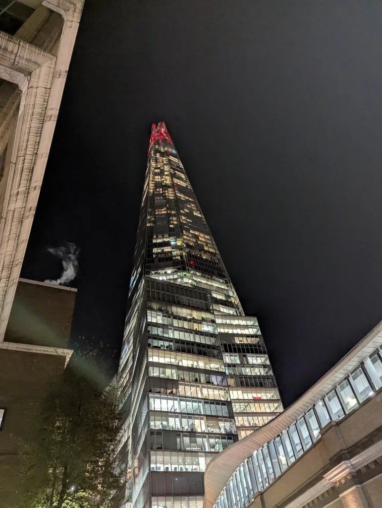 Low-angle view of The Shard glowing at night, its glass facade lit up from within, tapering to a red-lit tip against a black sky.