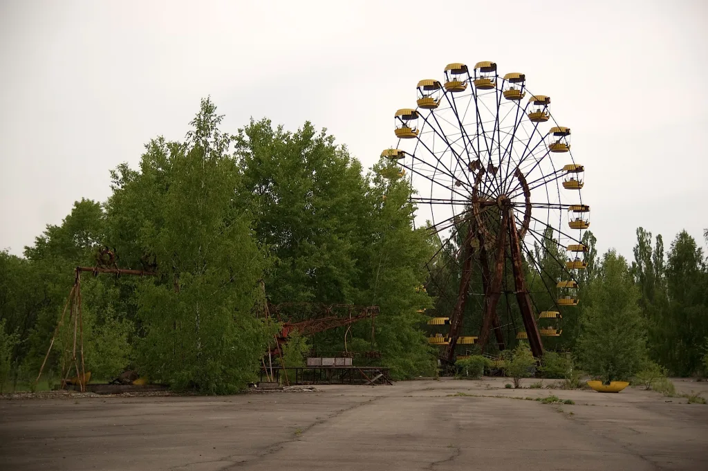 Abandoned Ferris wheel with yellow gondolas standing amidst overgrown trees in the derelict Pripyat amusement park.