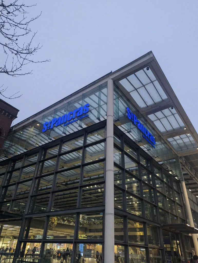 The modern glass and steel corner of St Pancras International station with blue lit signage under a twilight sky.