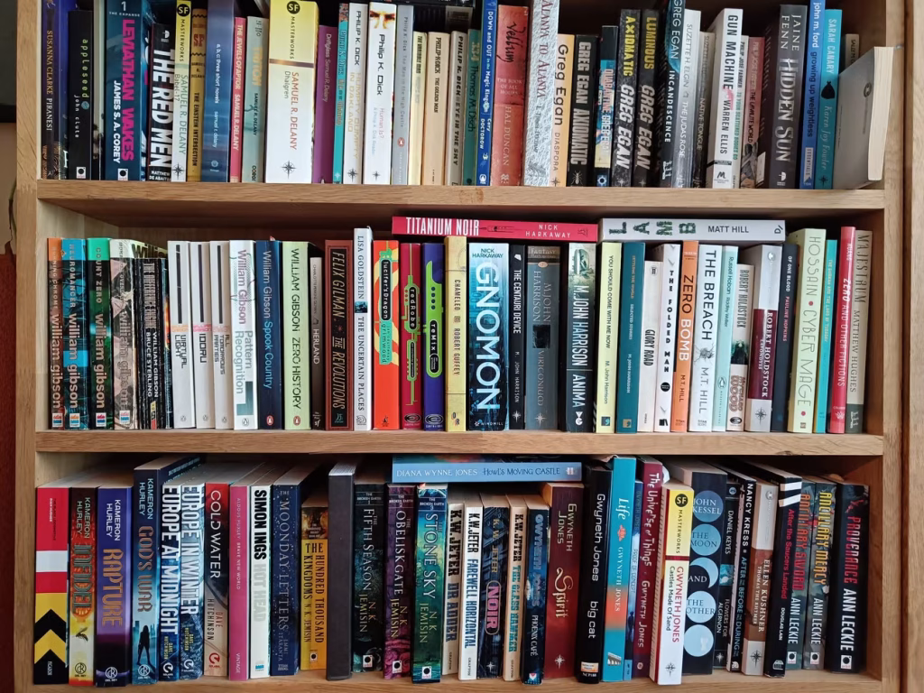 Three wooden shelves packed with science fiction and fantasy books by authors including William Gibson, N.K. Jemisin, and Samuel R. Delany.