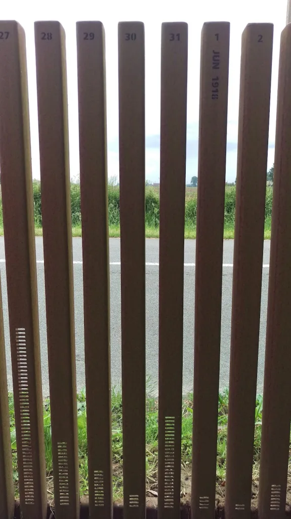 Vertical brown slats numbered 27 to 2. One is marked 1 JUN 1918. Horizontal notches at the base vary in height against a roadside background.