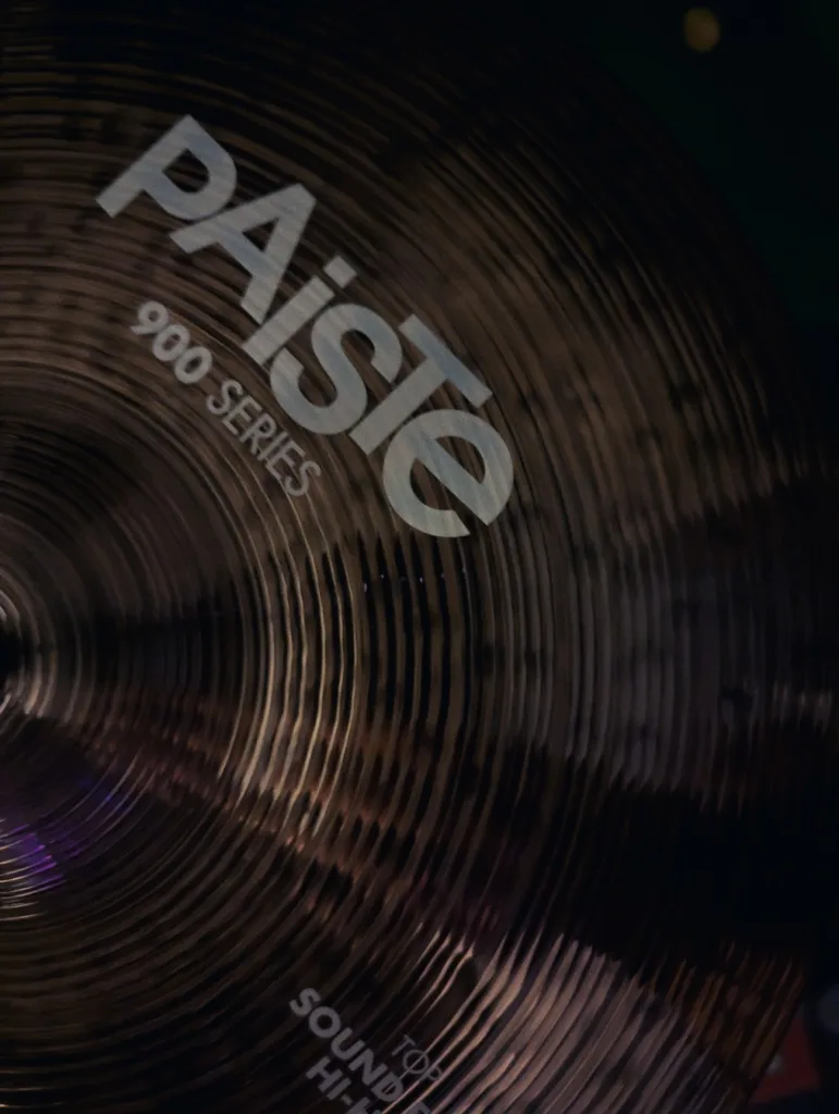 A bronze Paiste 900 Series hi-hat cymbal with prominent circular lathing and white brand text in low light.