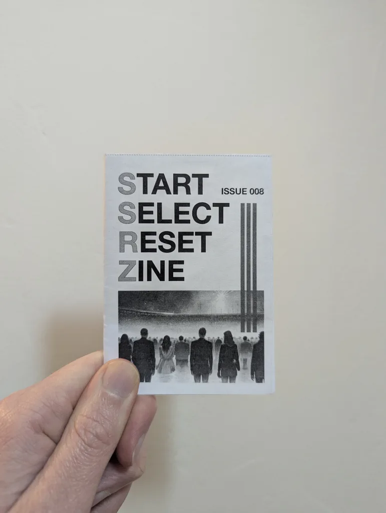 Featured image for Start Select Reset Zine Issue 008 - a hand holding a small black and white zine featuring a crowd in a stadium.