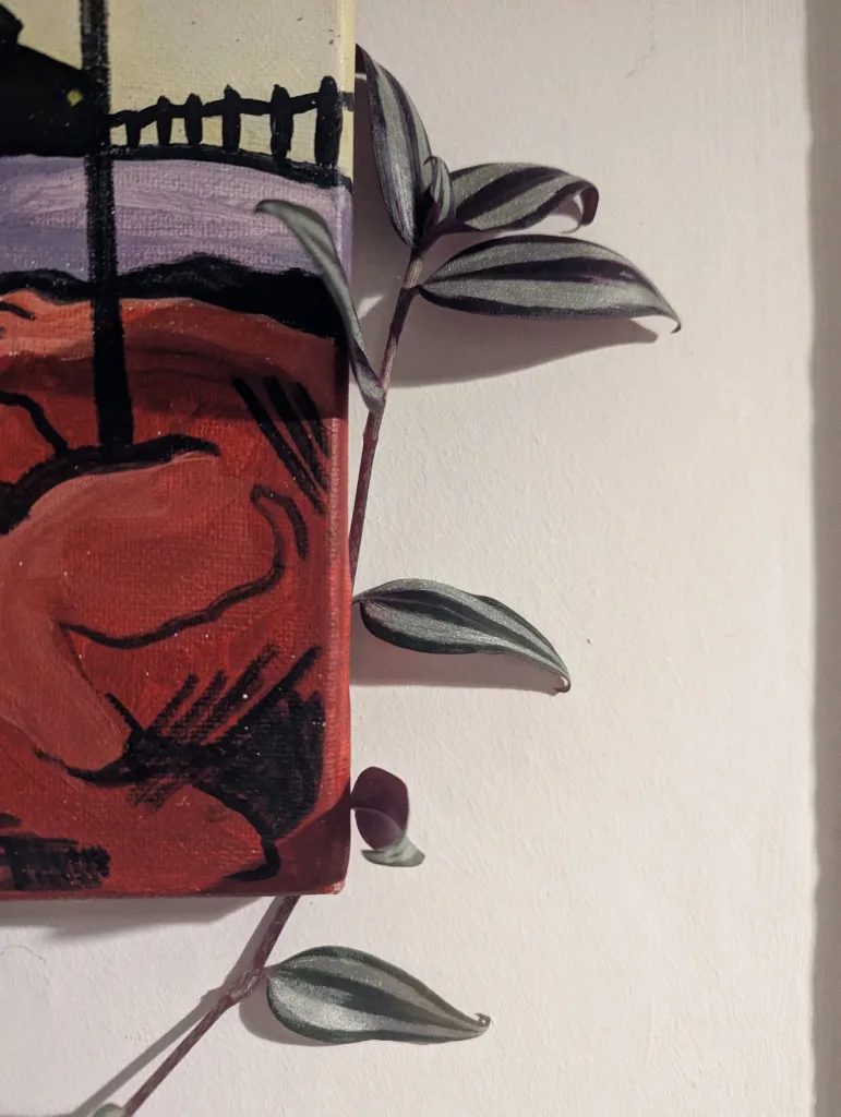 Purple and silver striped Tradescantia leaves peeking out from behind a small red, purple, and black canvas painting against a white wall.