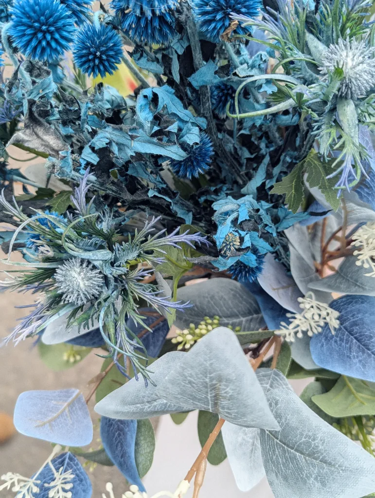 Close-up of a floral arrangement featuring bright blue globe thistles, dusty green eucalyptus leaves, and small white sprigs.