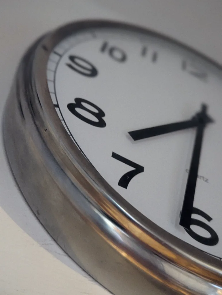 An angled close-up of a silver analog clock face with black numerals and hands, focusing on the numbers six through eight.