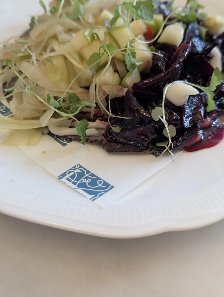 Dark roasted beetroot and shaved fennel salad topped with diced green apple and microgreens on a branded white plate.