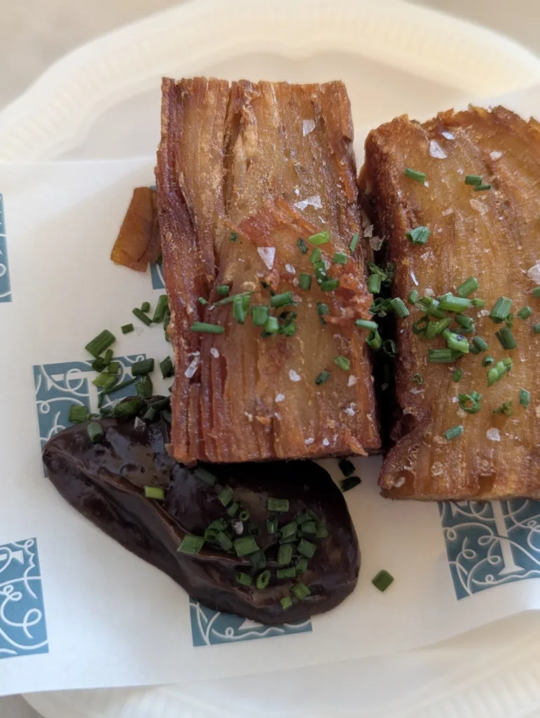 Golden-brown potato pavé rectangles topped with sea salt and chives, served with a dark sauce on a patterned paper liner.