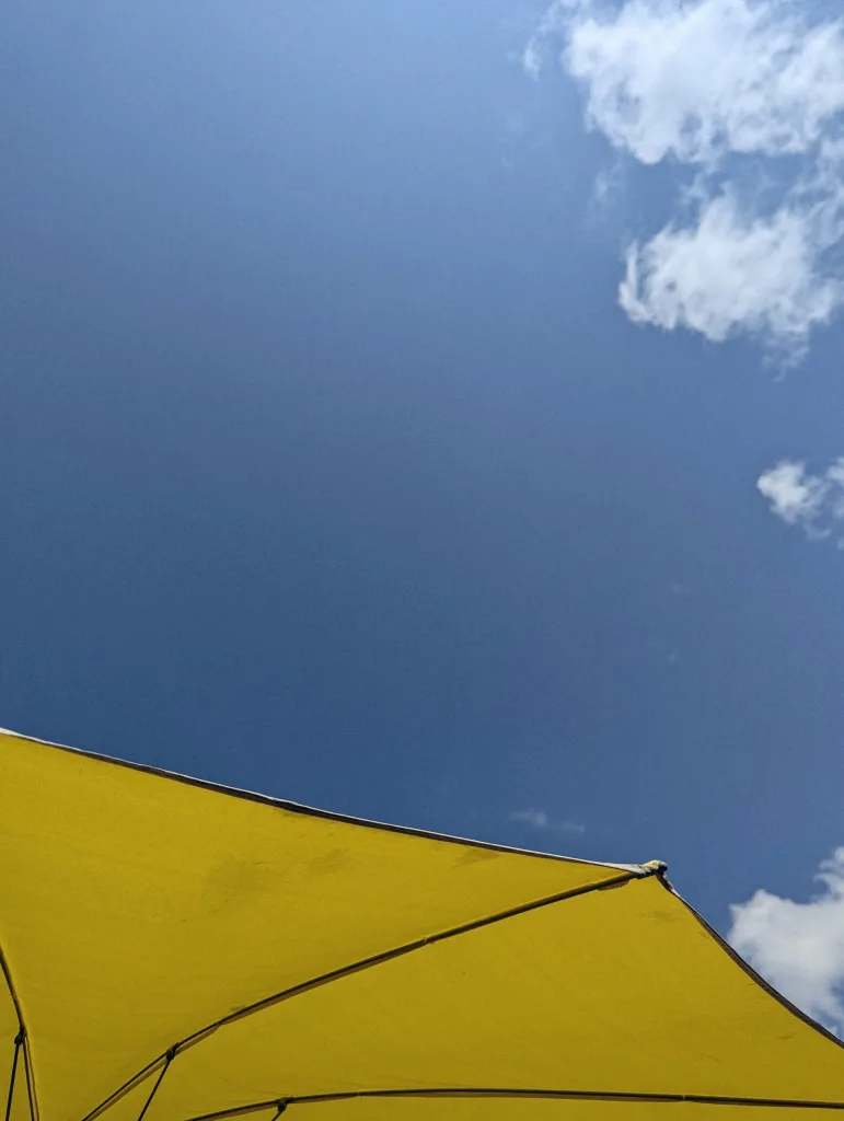 Underside of a bright yellow sun umbrella against a deep blue sky with wispy white clouds.