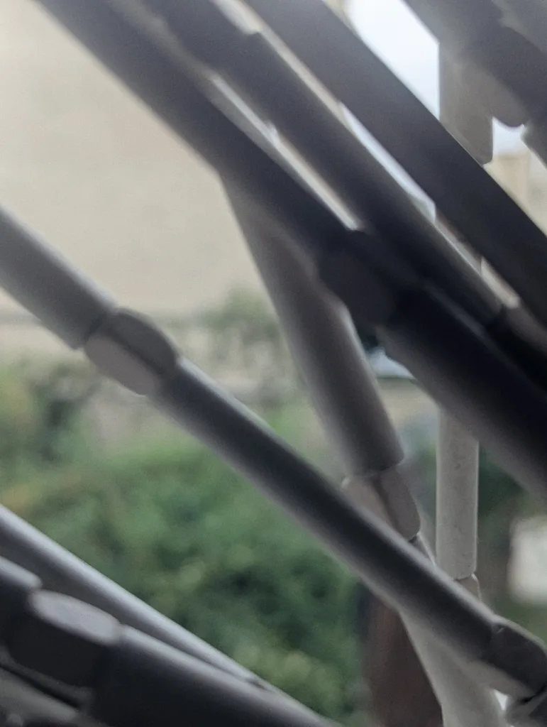 Diagonal grey beaded curtain in the foreground with a blurred background of green foliage and a beige building.