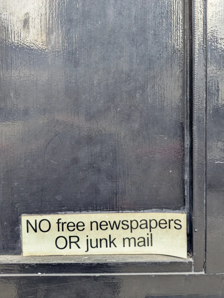 A small sign on a glossy black door reading: NO free newspapers OR junk mail.