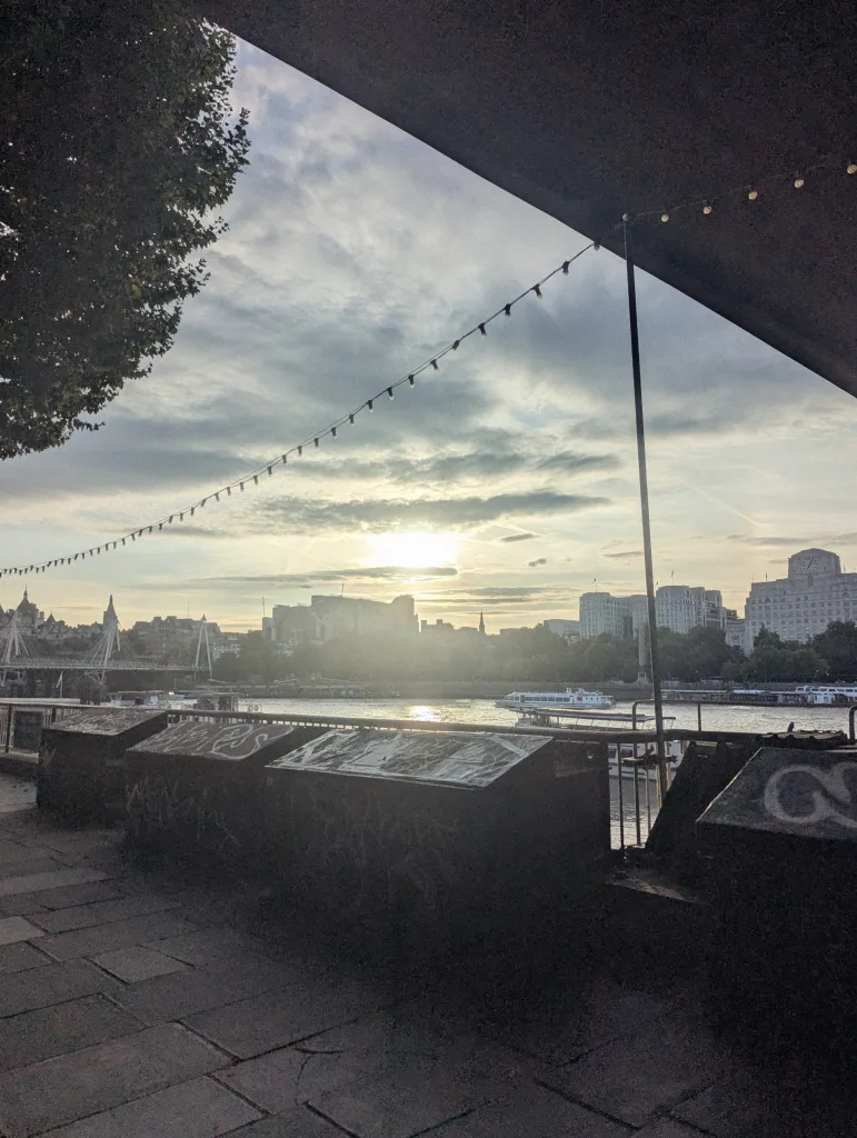 Sunset over the River Thames in London, framed by festoon lights and graffitied concrete planters on the South Bank.
