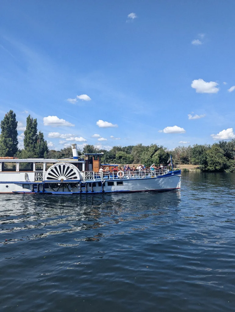 The Yarmouth Belle paddle steamer cruising on a river with passengers on deck under a bright blue sky with light clouds.