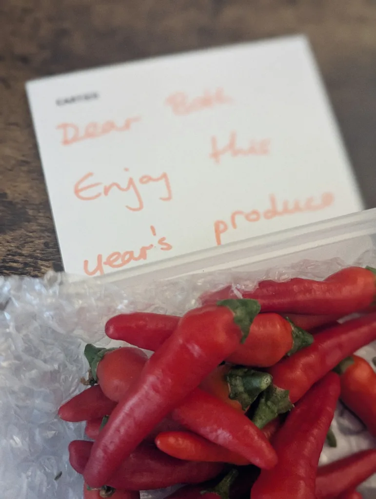 Small red chili peppers in a plastic tub next to a handwritten note reading: Dear Beth, Enjoy this year's produce.