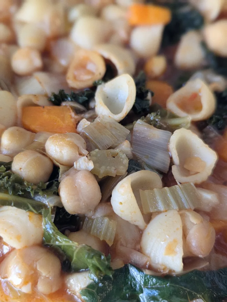 Close-up of a hearty soup with chickpeas, orecchiette pasta, kale, and celery in a light tomato broth.