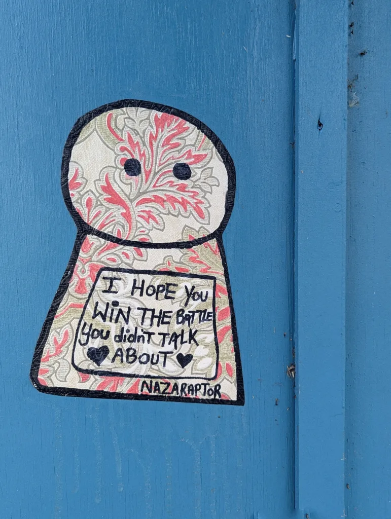 A patterned sticker on a blue wooden surface reading: I HOPE YOU WIN THE BATTLE YOU didn't TALK ABOUT by Nazaraptor.