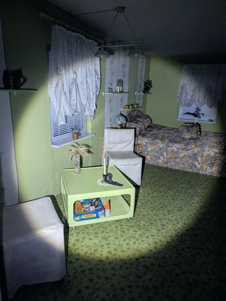 A retro room with lime green walls and patterned carpet, featuring a matching coffee table and white chairs illuminated by a harsh spotlight.
