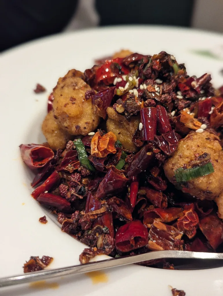 Crispy fried tofu nuggets covered in a mountain of dried red chilies, Sichuan peppercorns, and sesame seeds on a white plate.