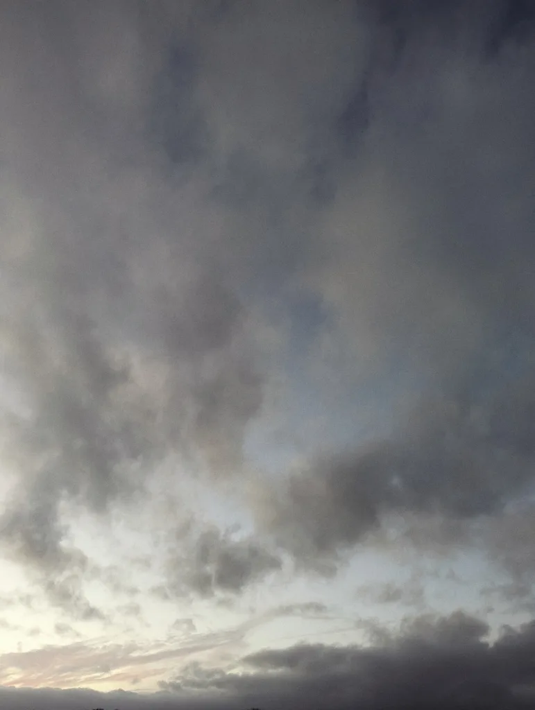 Heavy grey and white clouds filling the frame with a faint sliver of pink and yellow sunset light along the bottom horizon.